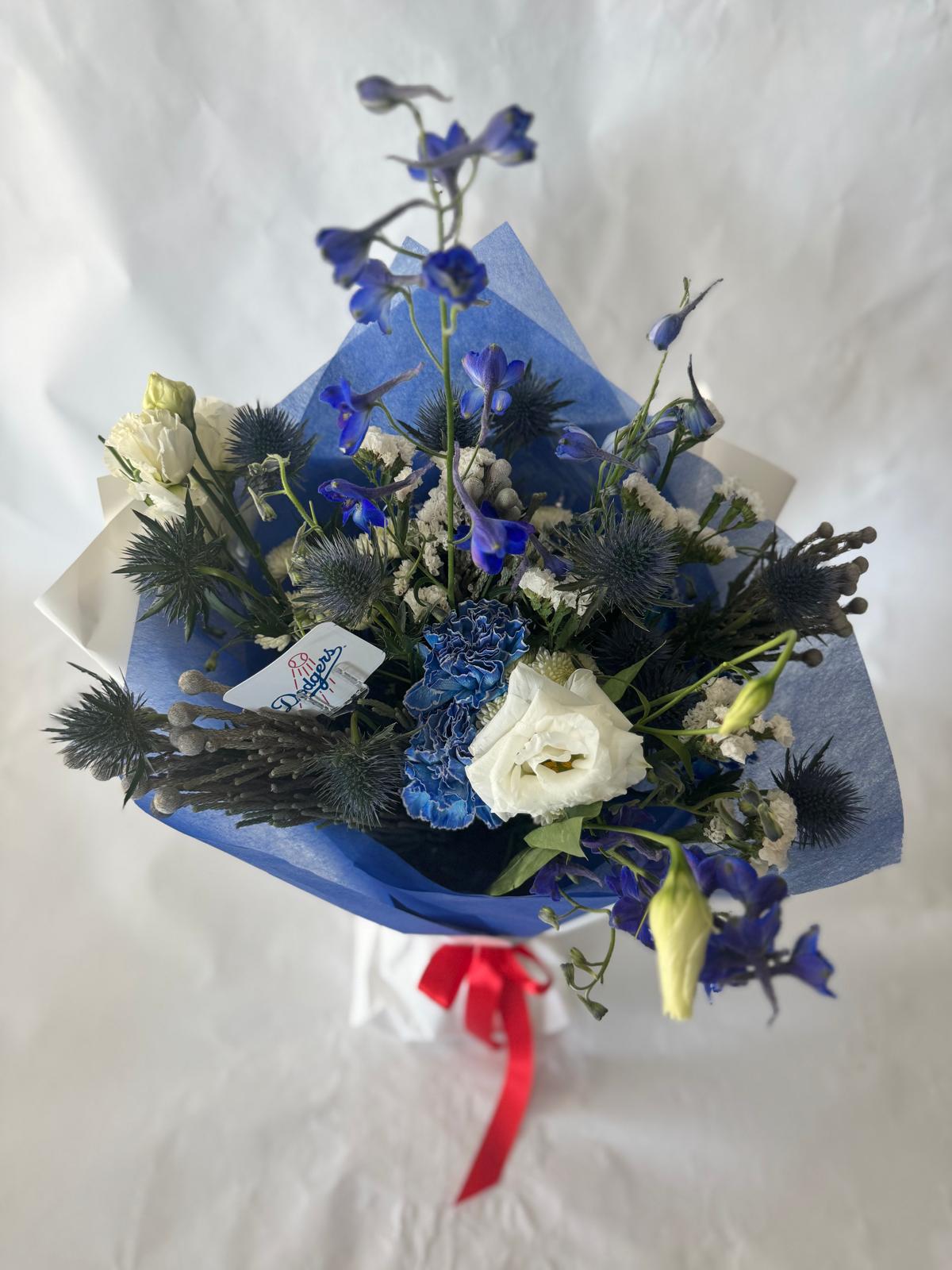 Signature floral bouquet in Dodgers team colors, wrapped in Korean paper and tied with a silk ribbon. Features blue, white, and soft neutral blooms with matching team sticker