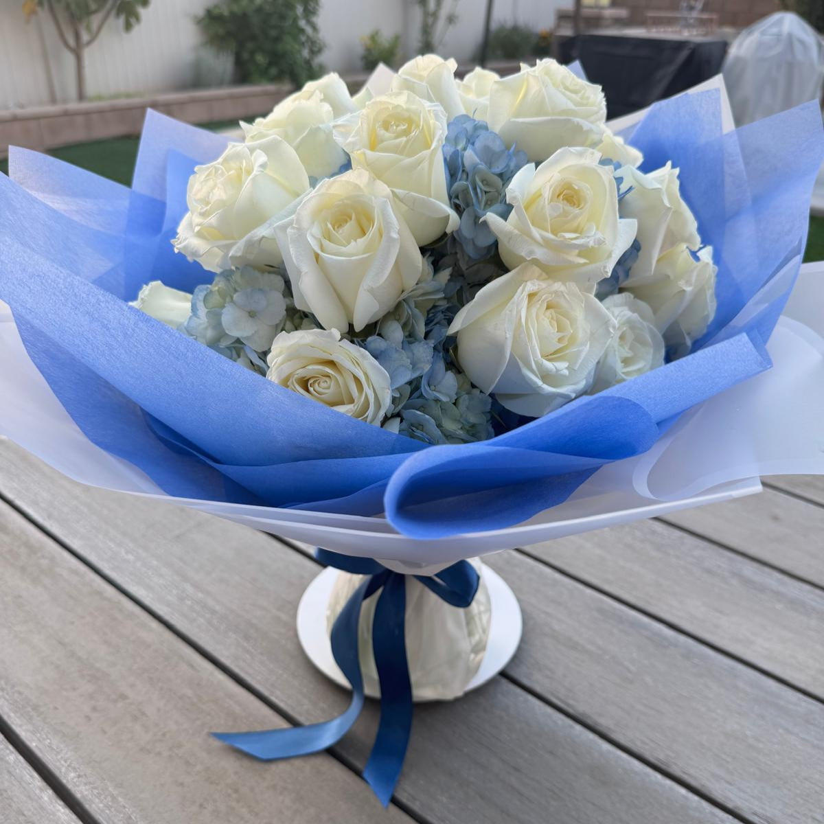 Blue and white bouquet with roses and hydrangeas, wrapped in designer paper with bold blue accents.