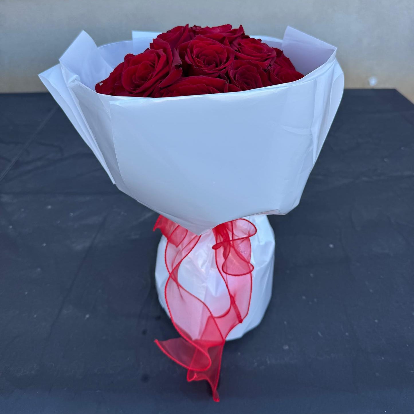 Classic red rose bouquet wrapped in white paper with a soft red ribbon.