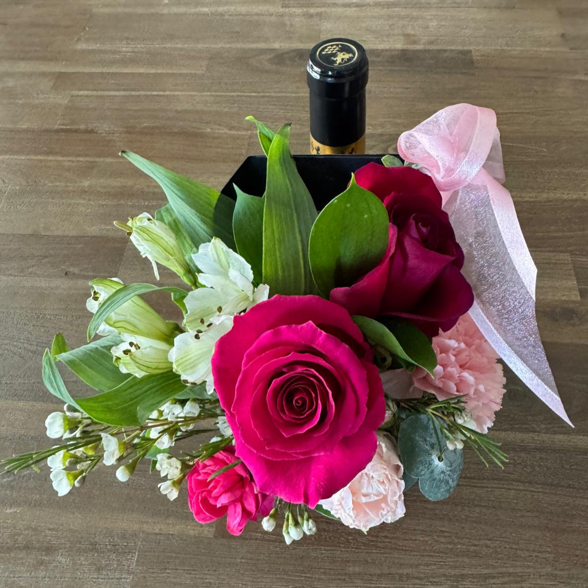 Custom floral party favor in a gift carrier with roses, carnations, and ribbon.