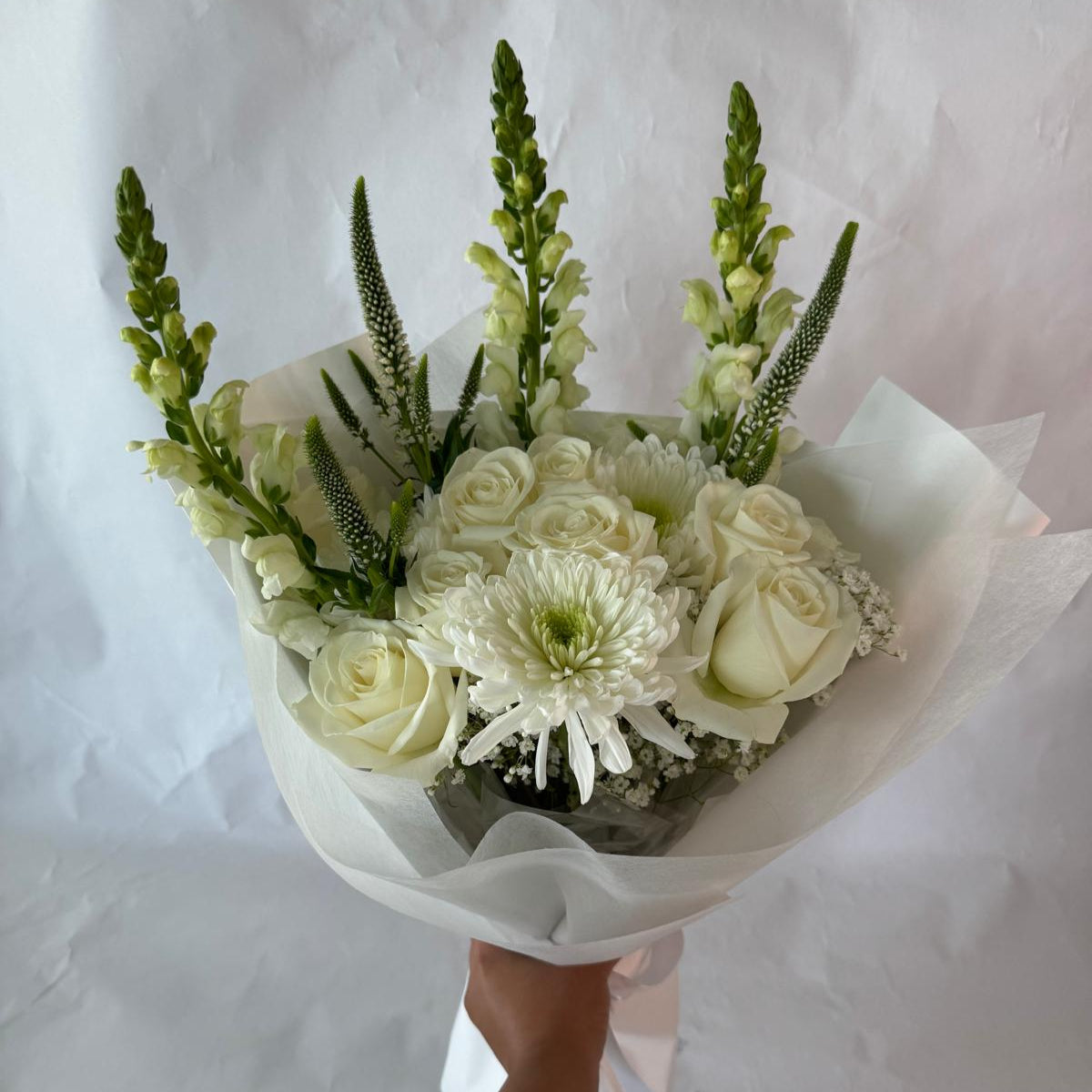 An elegant all-white bouquet wrapped in sheer white paper, symbolizing peace, purity and everlasting light, offered as a gentle tribute in times of remembrance.