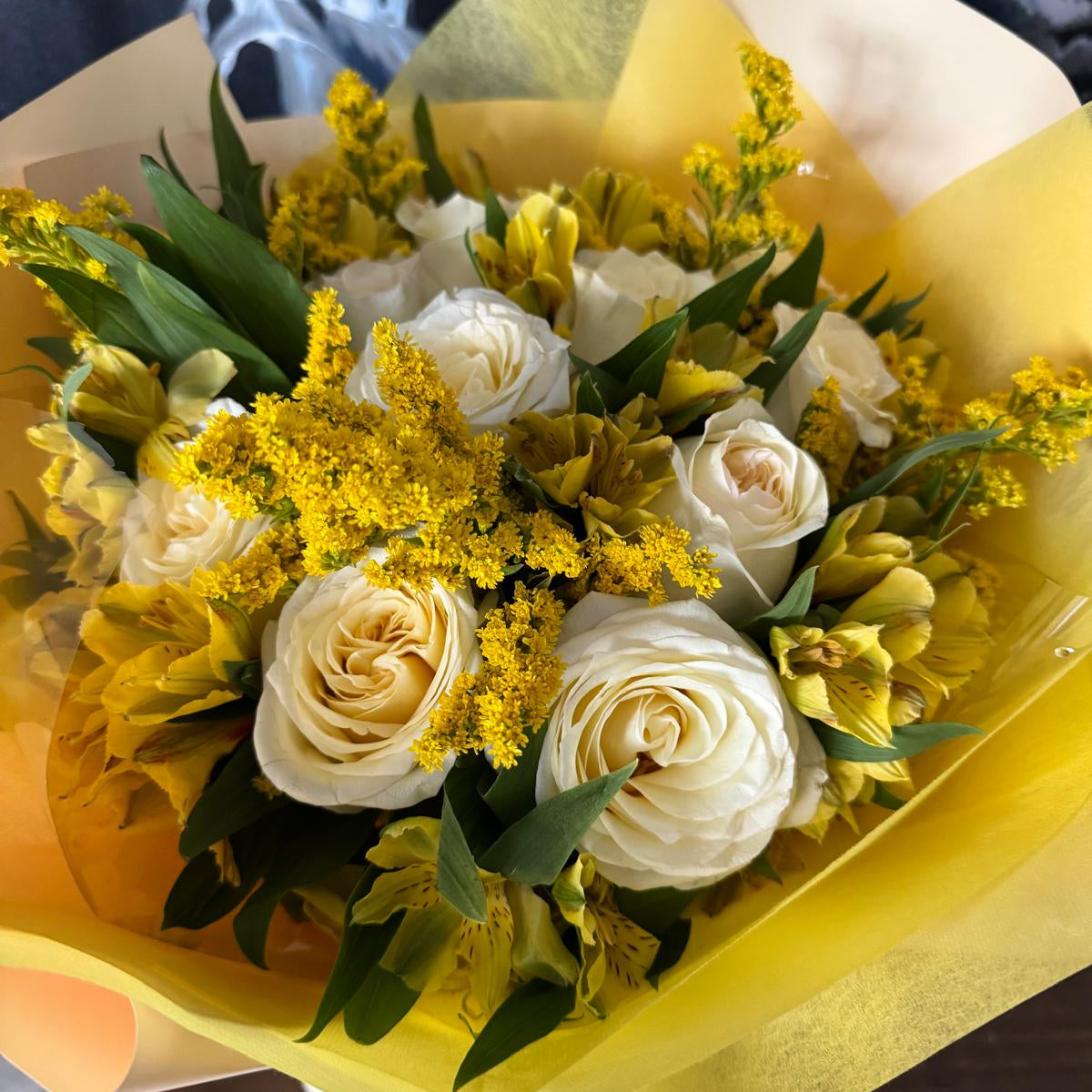 Golden Daylight Bouquet in one size only featuring creamy white roses, yellow alstroemeria, and golden accents wrapped in yellow paper by Nai Pascoal Bouquets