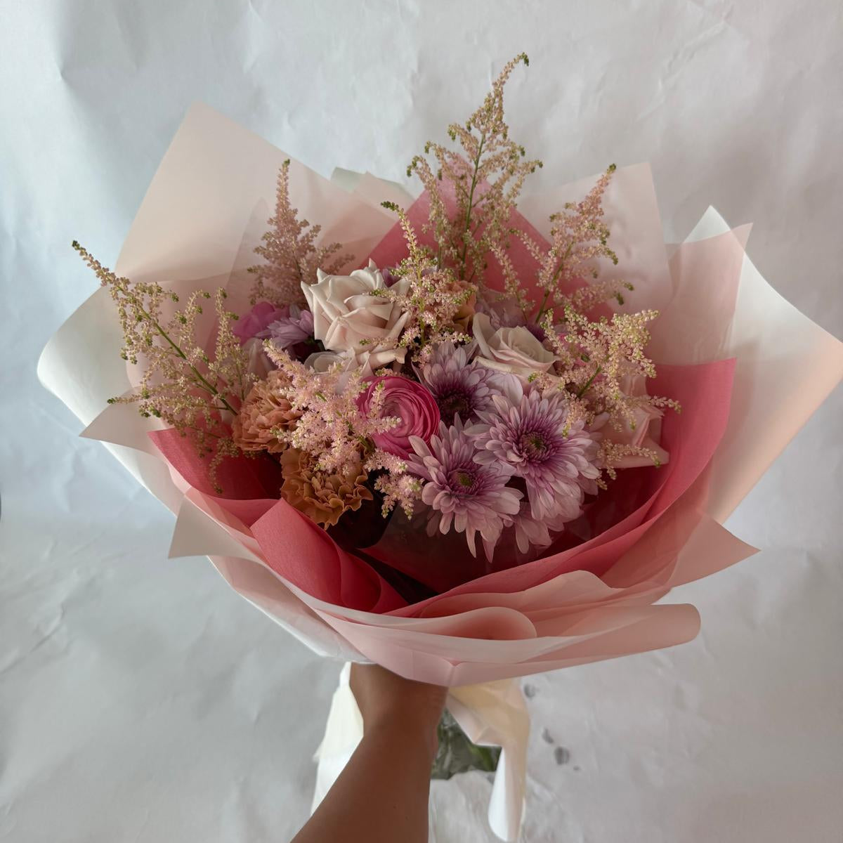 A gentle bouquet in warm blush and rose tones, softly wrapped in pink and cream, offering warmth and compassion during moments of grief.