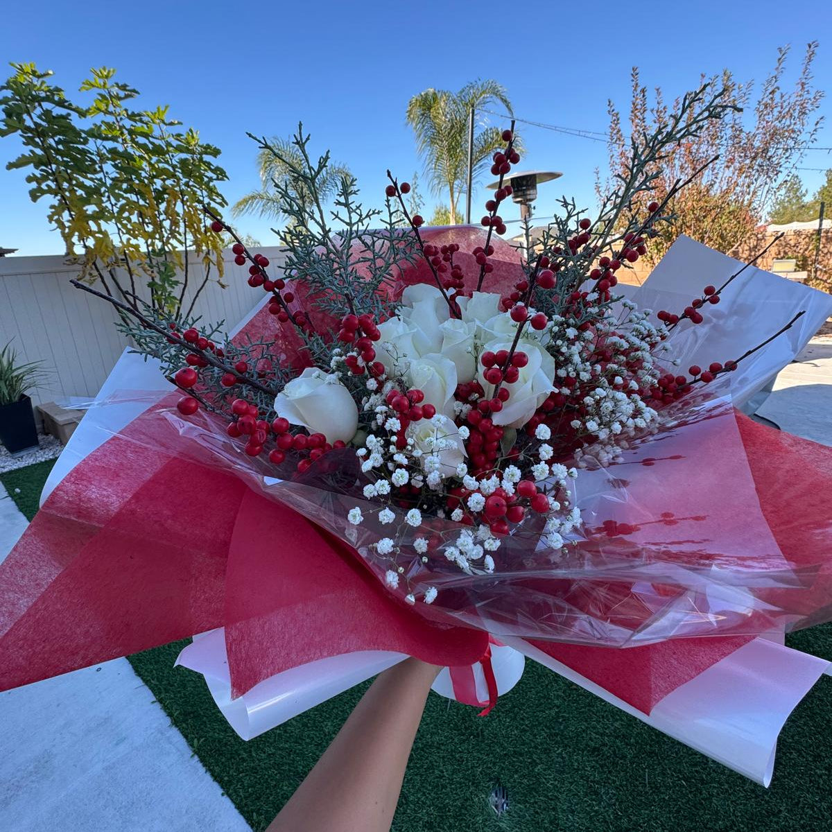 Christmas bouquet with white roses, red berries, baby’s breath, and winter greenery wrapped in red and white paper – Holiday Cheer by Nai Pascoal Bouquets.