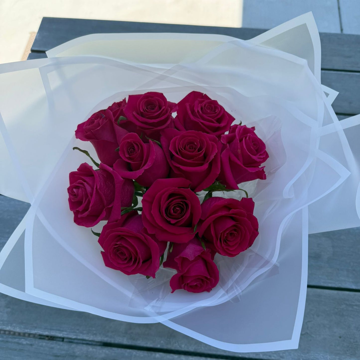 Bouquet of 12 hot pink roses wrapped in white paper with a satin ribbon.