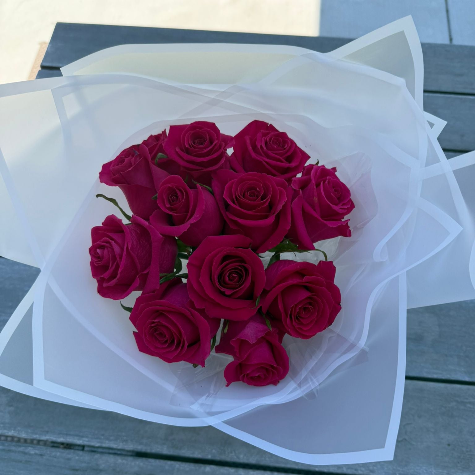 Bouquet of 12 hot pink roses wrapped in white paper with a satin ribbon.