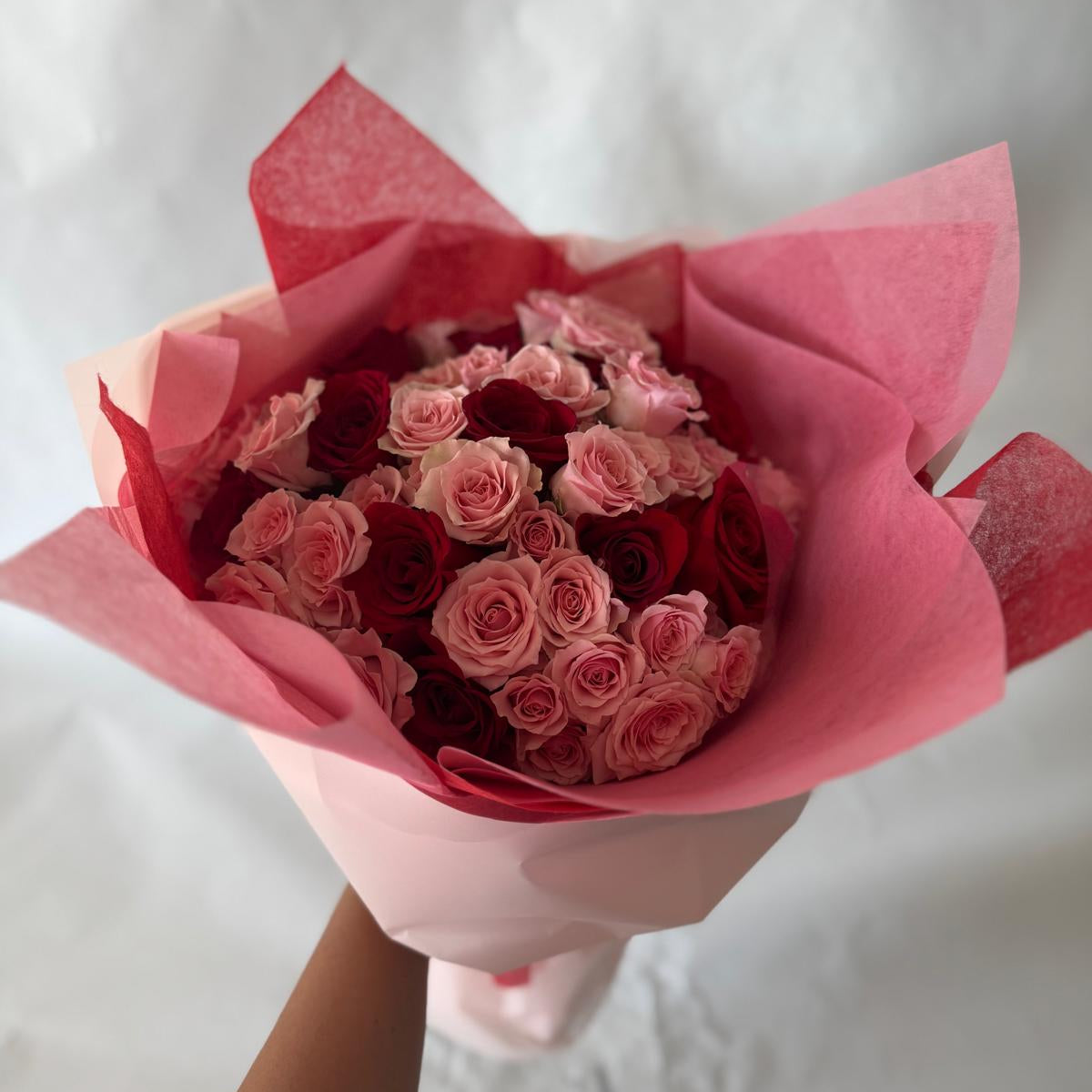 A hand-held bouquet of red and pink roses wrapped in red and pink tissue paper.