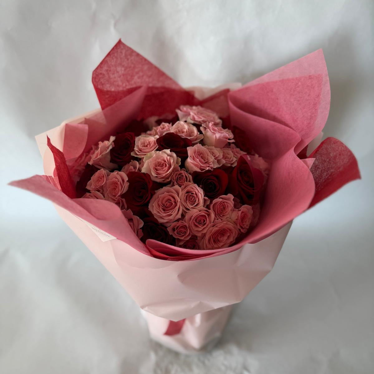 A bouquet of red and pink roses wrapped in red and pink tissue paper.
