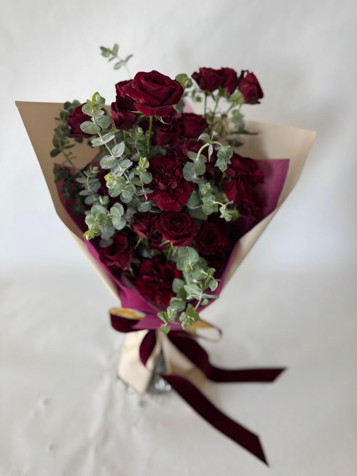 Burgundy bouquet with deep red roses and carnations, accented by eucalyptus and wrapped in plum paper with a rich, romantic look.