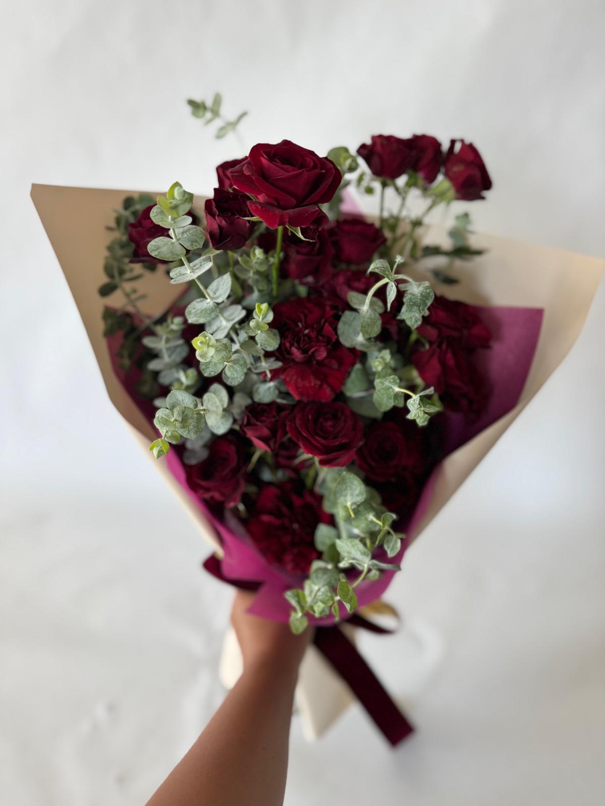 Burgundy bouquet with deep red roses and carnations, accented by eucalyptus and wrapped in plum paper with a rich, romantic look.
