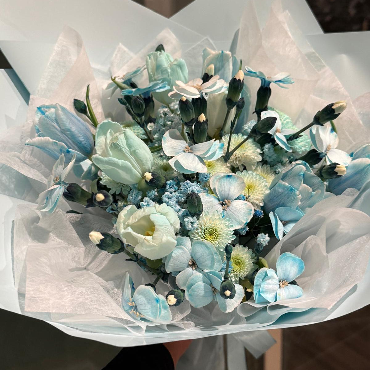 Aquamarine-inspired bouquet wrapped in soft ivory tissue and blue paper with satin ribbon.