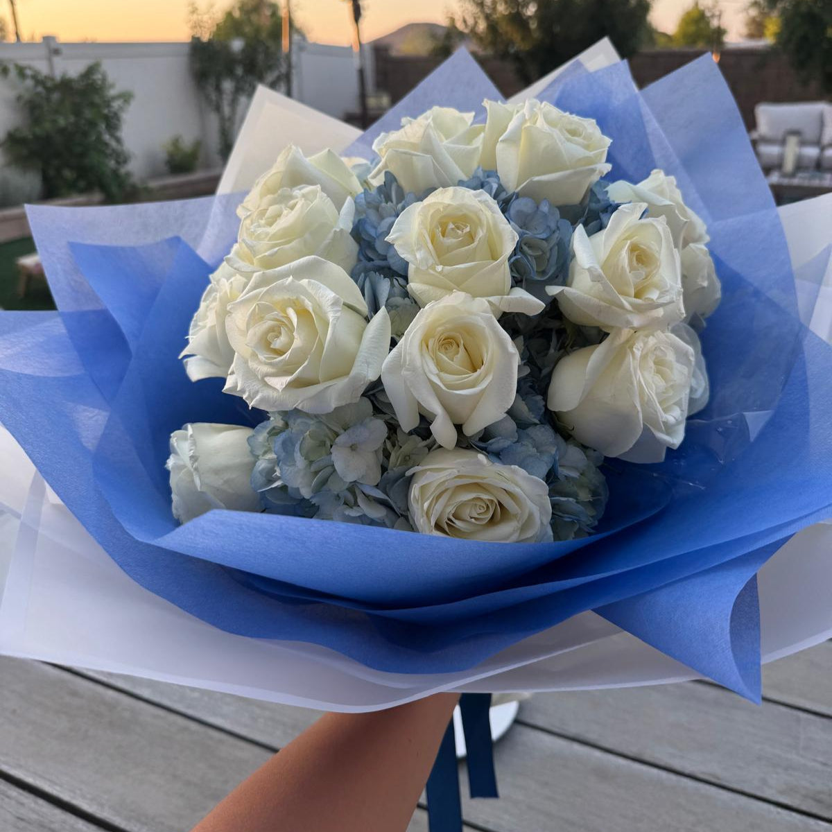 Blue and white bouquet with roses and hydrangeas, wrapped in designer paper with bold blue accents.