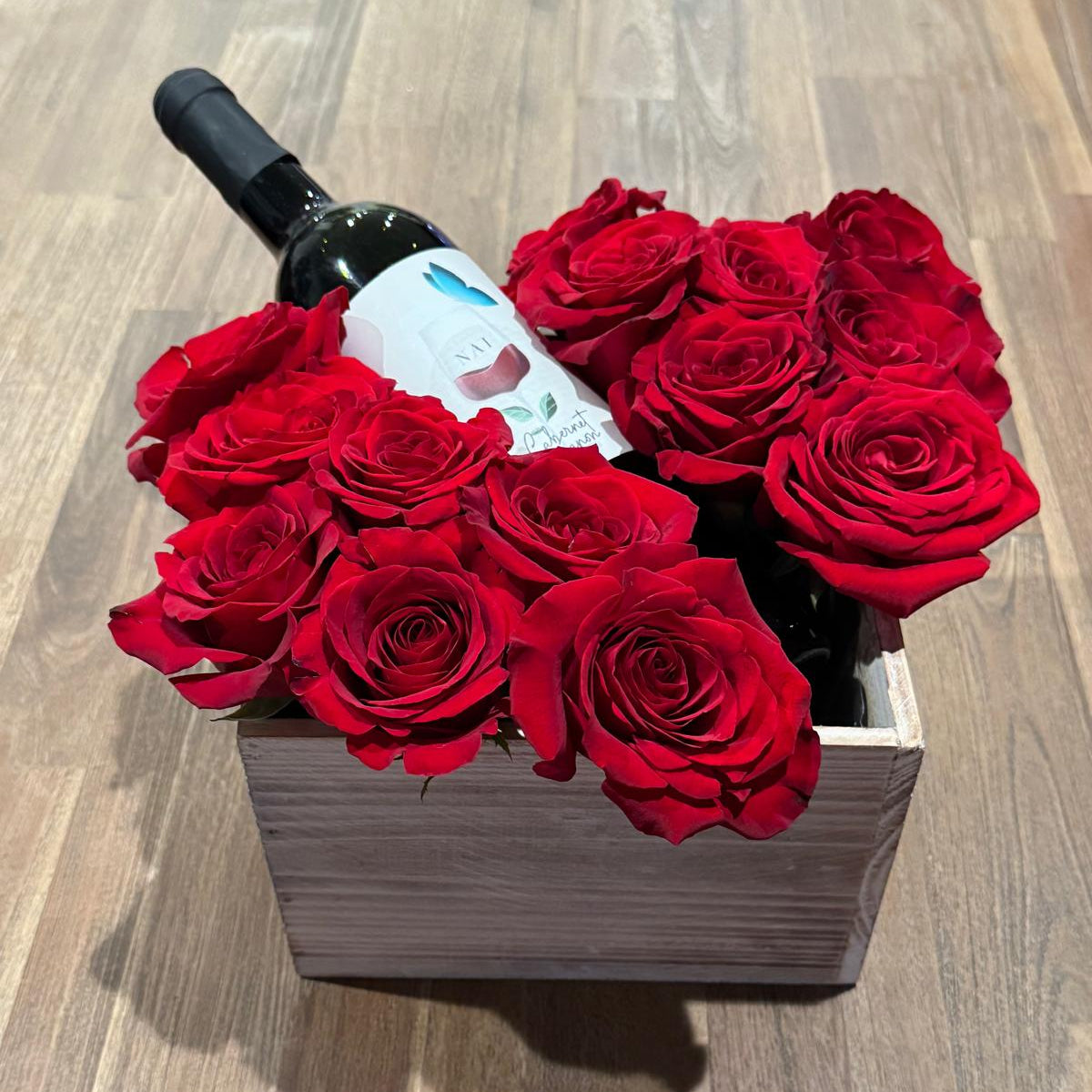 A romantic Valentine’s arrangement featuring premium red roses styled around a wine bottle in a keepsake wooden box. Handcrafted and available for local delivery.