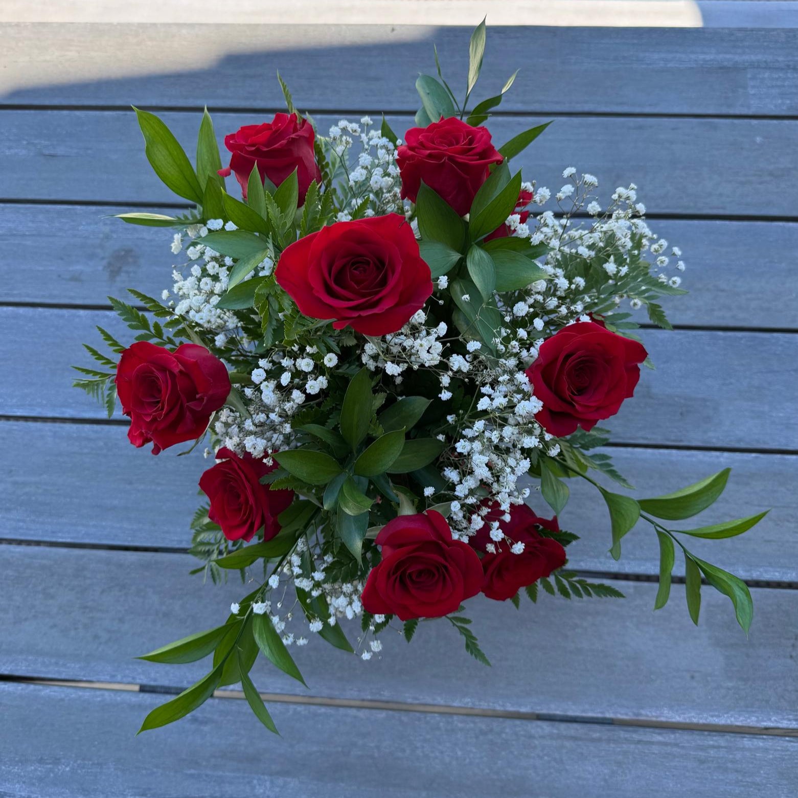 Elegant vase arrangement of 12 red roses with baby’s breath and greenery, finished with a red bow.