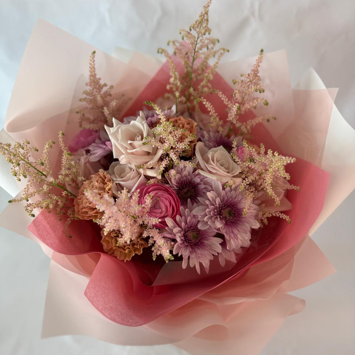 A gentle bouquet in warm blush and rose tones, softly wrapped in pink and cream, offering warmth and compassion during moments of grief.