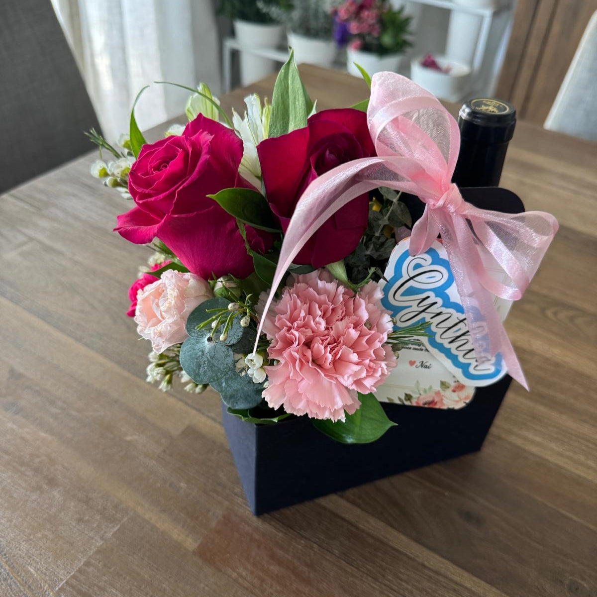 Custom floral party favor in a gift carrier with roses, carnations, and ribbon.