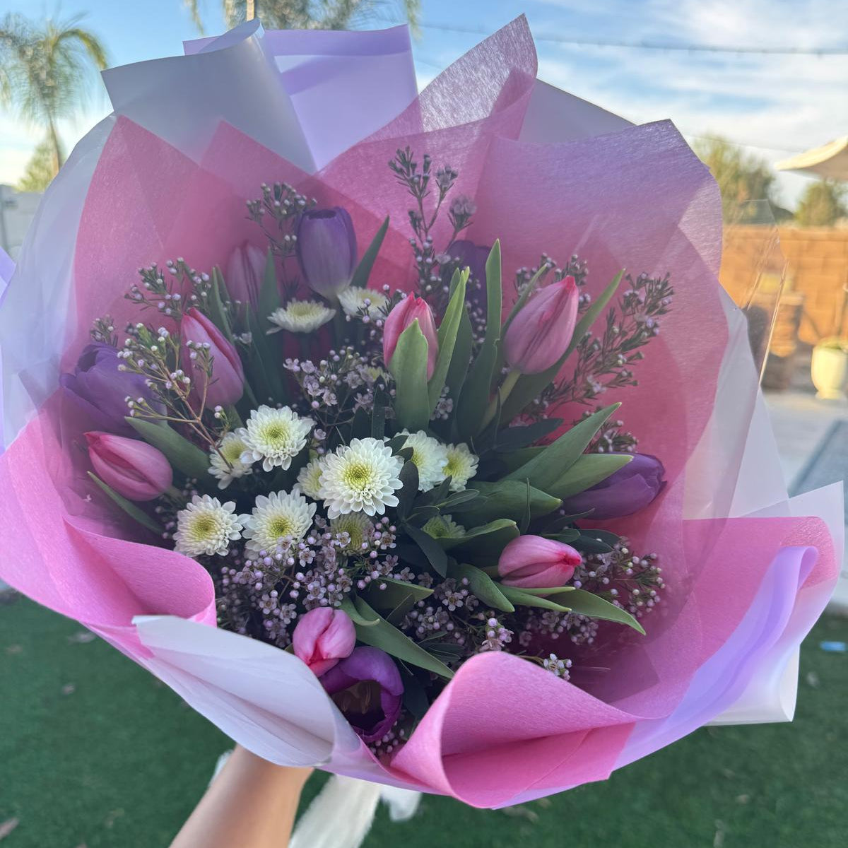 Spring bouquet with pink and lavender tulips, white chrysanthemums, and wax flower wrapped in blush and lilac pastel paper.
