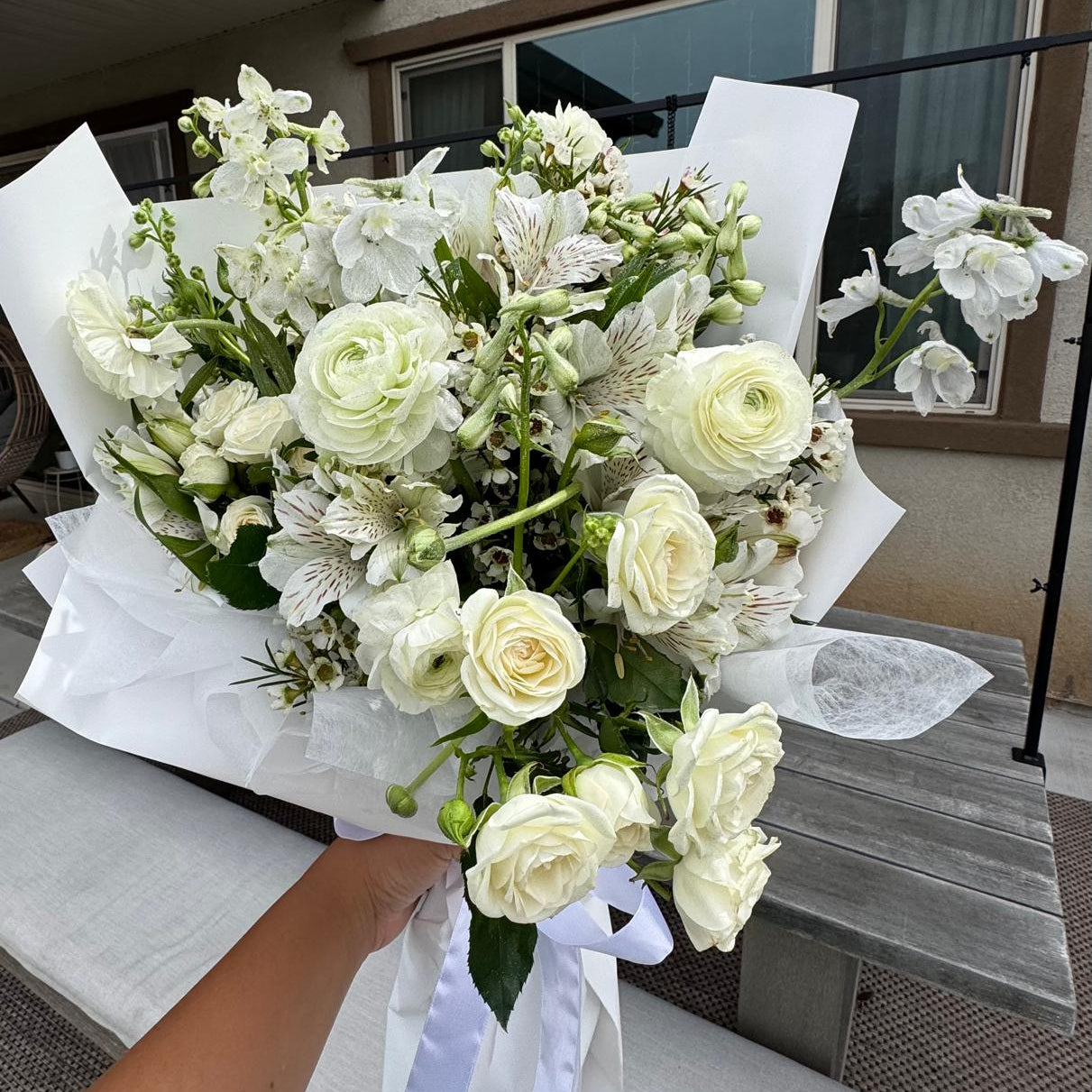 April Diamond bouquet featuring soft white roses, ranunculus, and delicate blooms, elegantly wrapped in white paper with a ribbon.