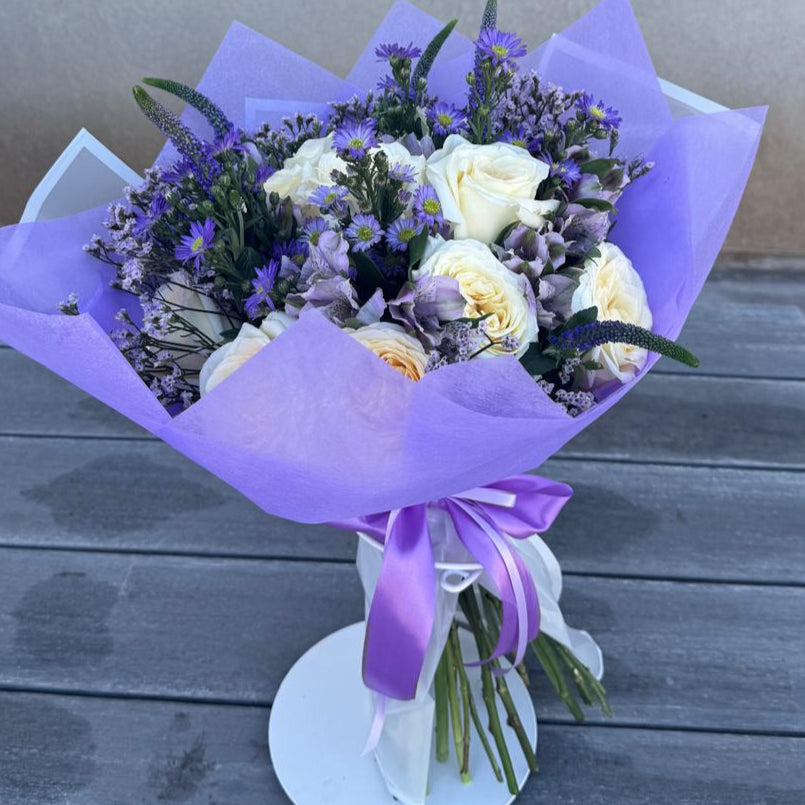 Elegant bouquet of ivory roses and violet flowers with lavender accents, wrapped in lilac paper, symbolizing Athena’s wisdom and strength.