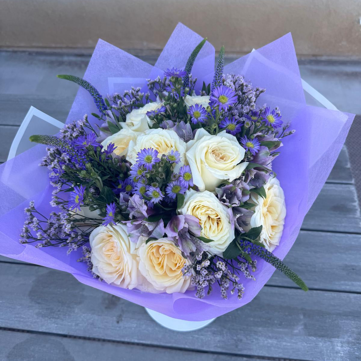 Elegant bouquet of ivory roses and violet flowers with lavender accents, wrapped in lilac paper, symbolizing Athena’s wisdom and strength.
