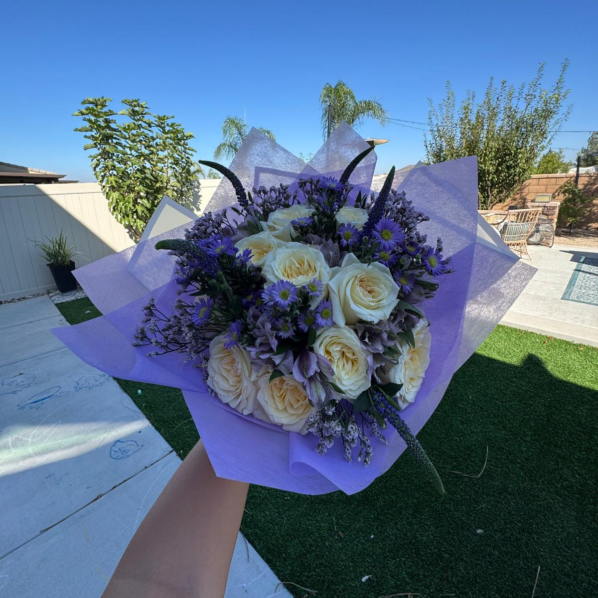 Elegant bouquet of ivory roses and violet flowers with lavender accents, wrapped in lilac paper, symbolizing Athena’s wisdom and strength.