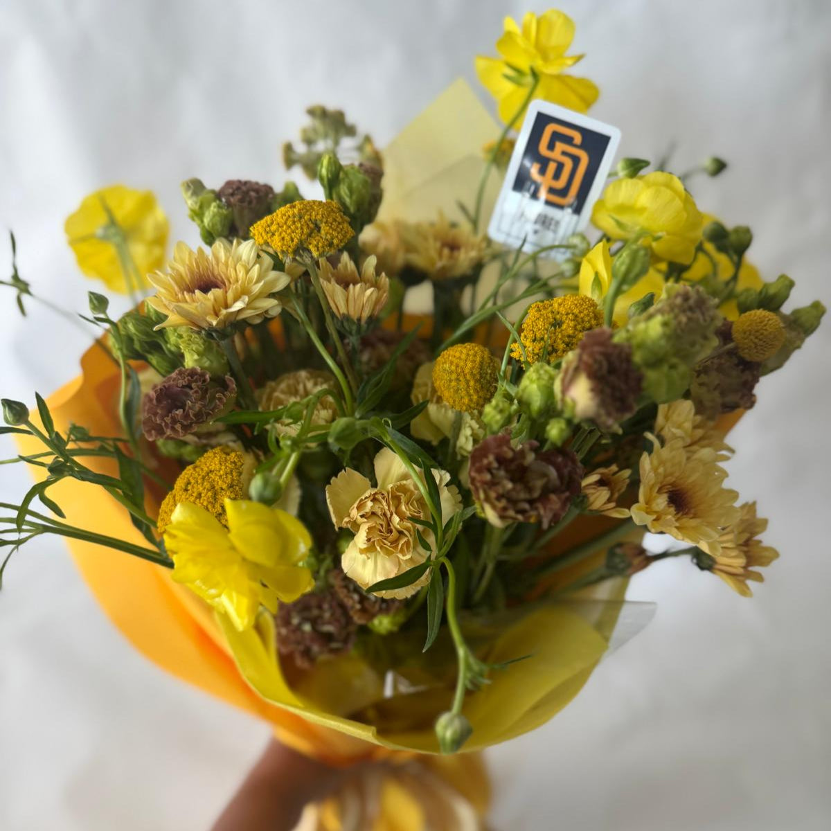 Signature floral bouquet inspired by the Padres, featuring rich brown, gold, and cream blooms. Wrapped in Korean paper with a silk ribbon and matching team sticker.