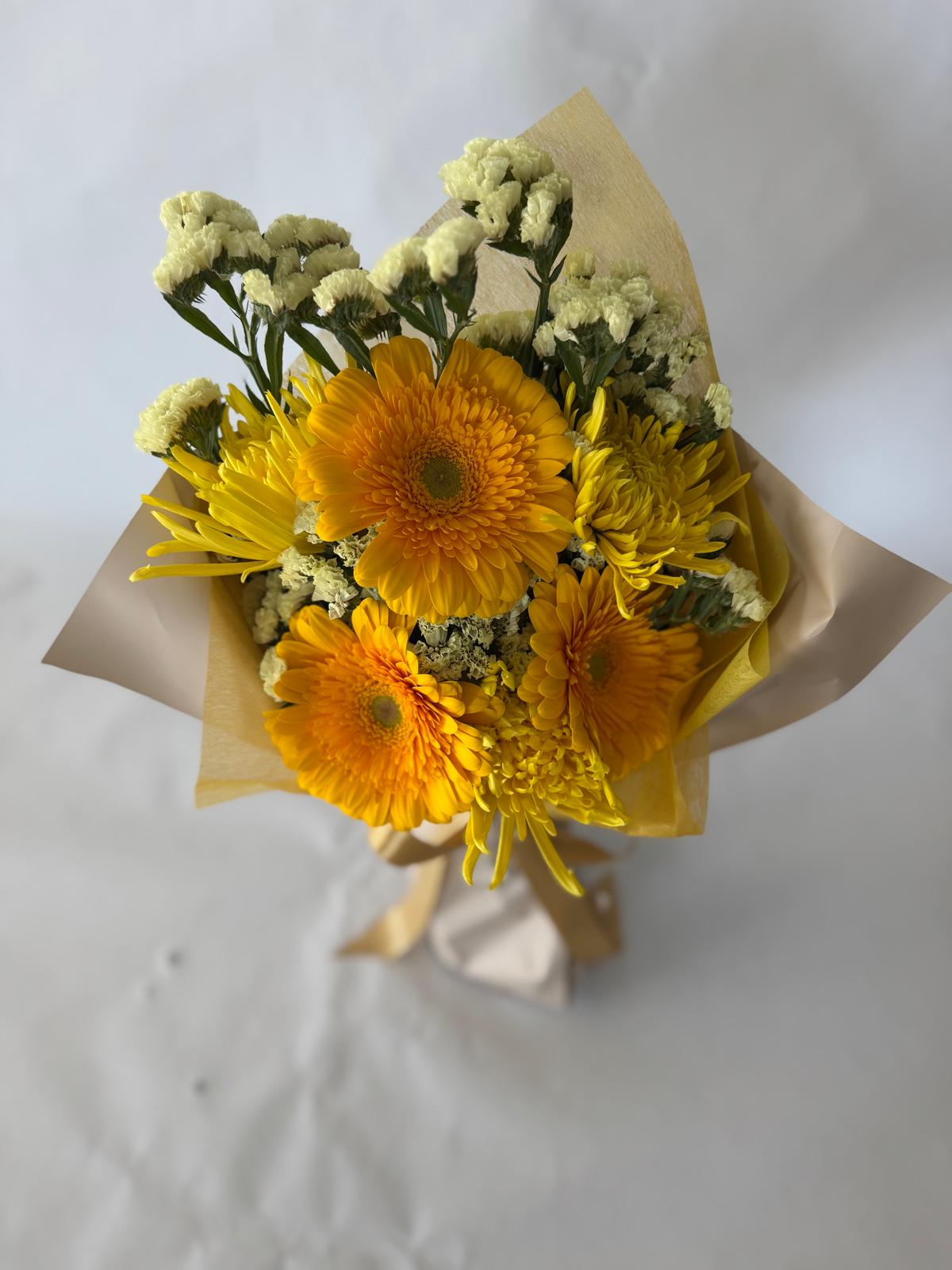 Yellow bouquet with bright, sunlit flowers in soft butter and lemon tones, hand-wrapped in signature floral paper.