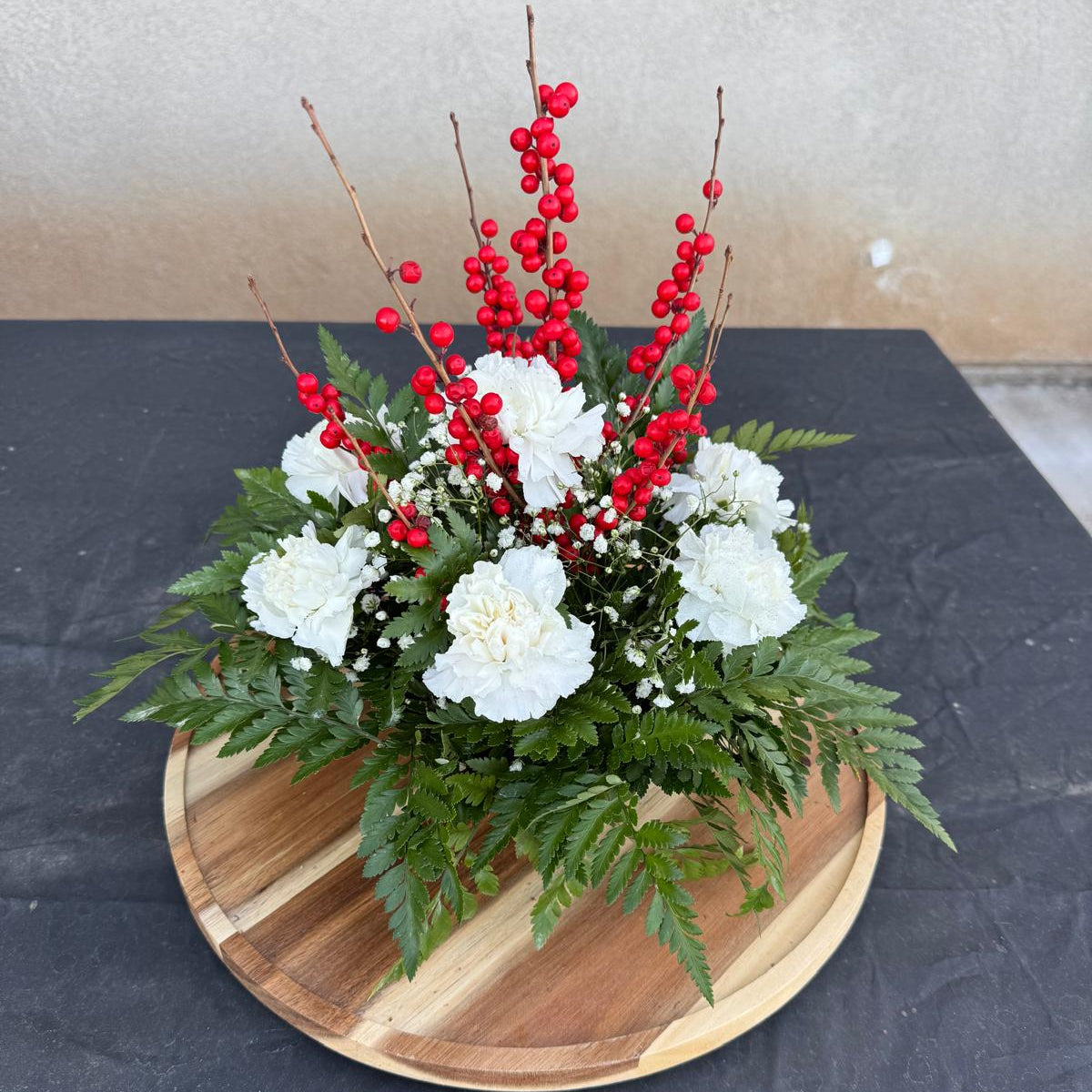 Christmas centerpiece with white flowers, red berries, baby’s breath, and greenery arranged in a low round base — Merry & Bright by Nai Pascoal Bouquets.