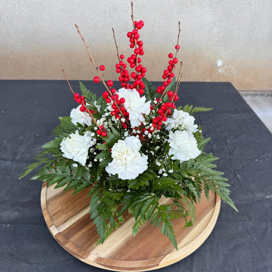 Christmas centerpiece with white flowers, red berries, baby’s breath, and greenery arranged in a low round base — Merry & Bright by Nai Pascoal Bouquets.