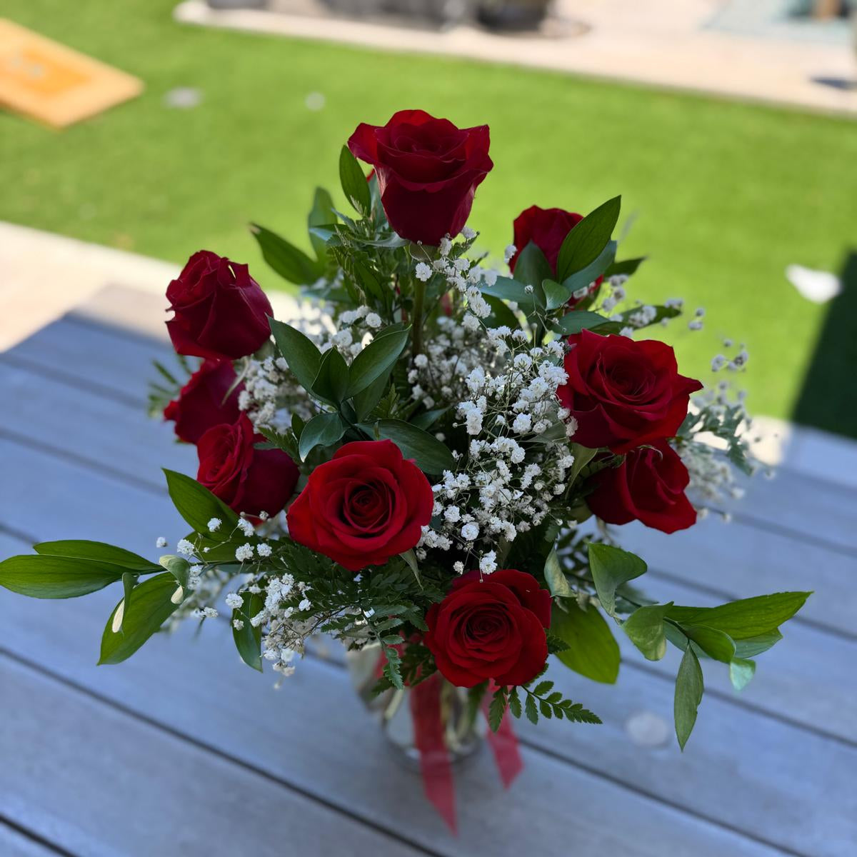 Elegant vase arrangement of 12 red roses with baby’s breath and greenery, finished with a red bow.