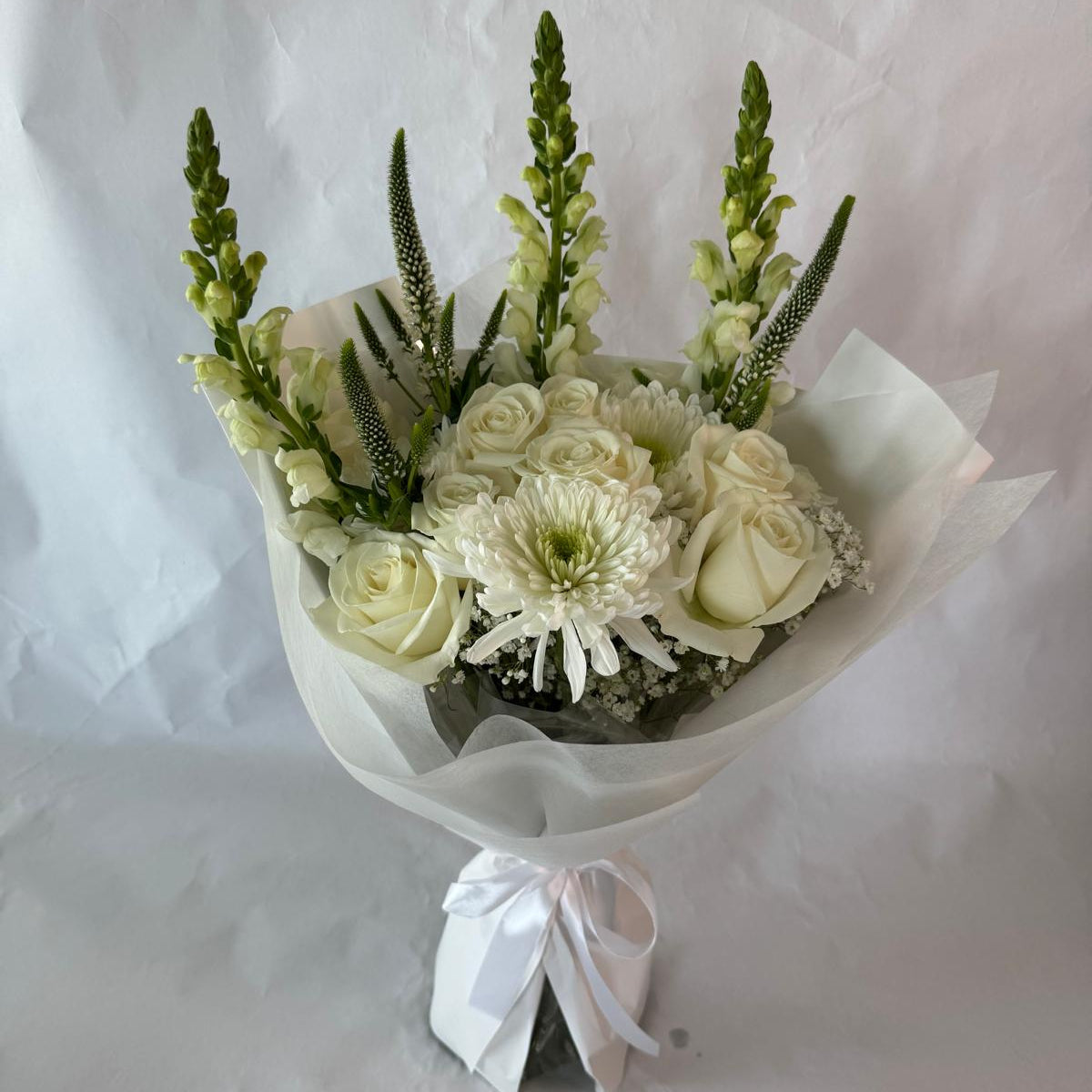 An elegant all-white bouquet wrapped in sheer white paper, symbolizing peace, purity and everlasting light, offered as a gentle tribute in times of remembrance.
