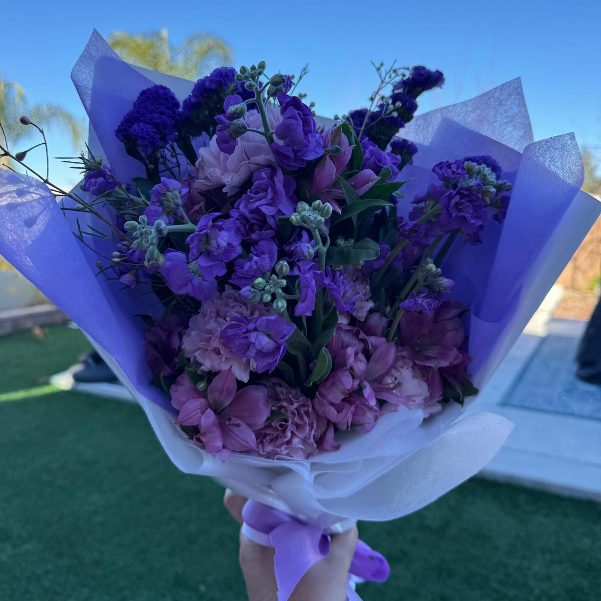 Purple and lavender February bouquet featuring stock, carnations, alstroemeria, and statice wrapped in soft lavender paper.