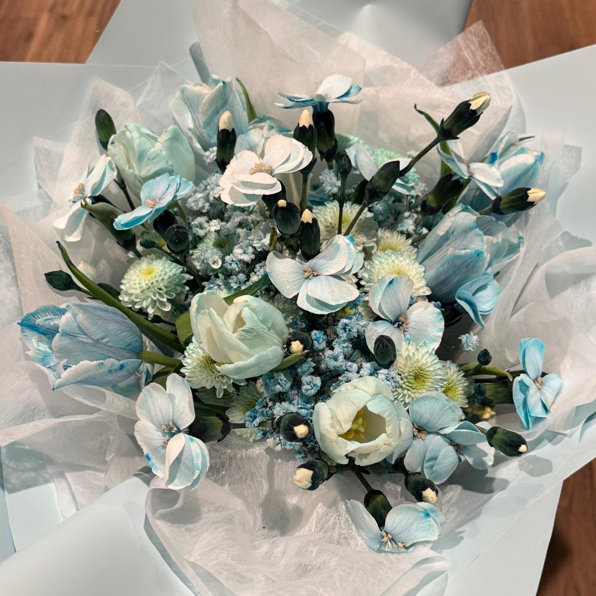 Aquamarine-inspired bouquet wrapped in soft ivory tissue and blue paper with satin ribbon.