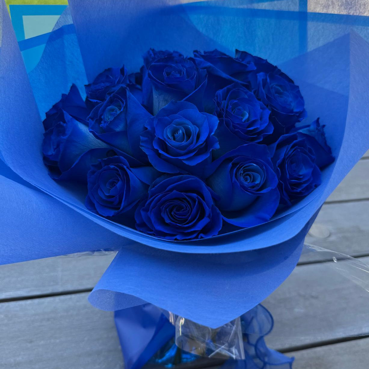 Hand-tied bouquet of deep sapphire-blue roses wrapped in blue matte paper with a satin ribbon.