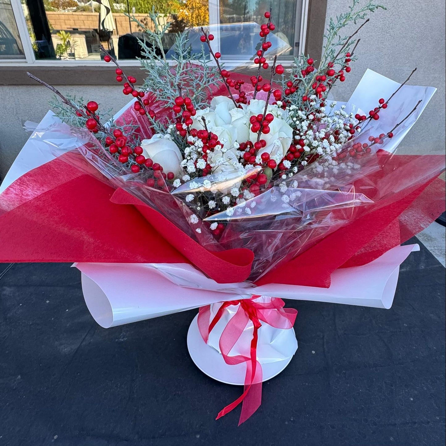 Christmas bouquet with white roses, red berries, baby’s breath, and winter greenery wrapped in red and white paper – Holiday Cheer by Nai Pascoal Bouquets.