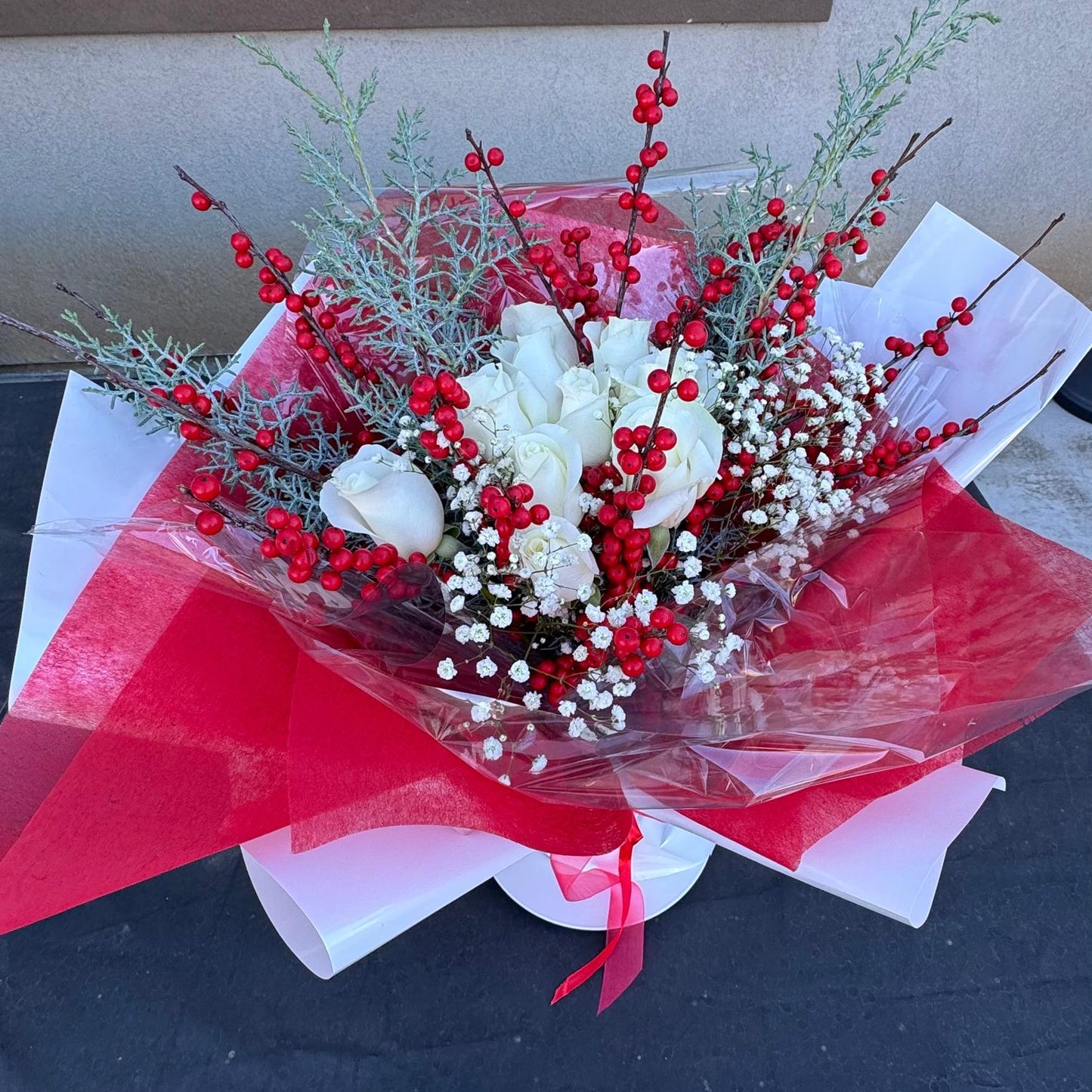 Christmas bouquet with white roses, red berries, baby’s breath, and winter greenery wrapped in red and white paper – Holiday Cheer by Nai Pascoal Bouquets.