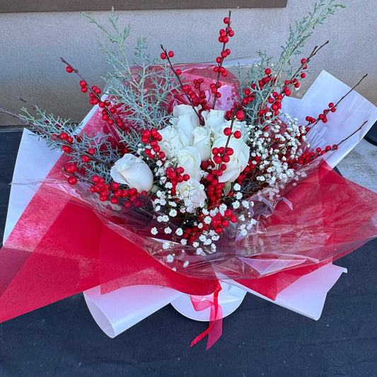 Christmas bouquet with white roses, red berries, baby’s breath, and winter greenery wrapped in red and white paper – Holiday Cheer by Nai Pascoal Bouquets.