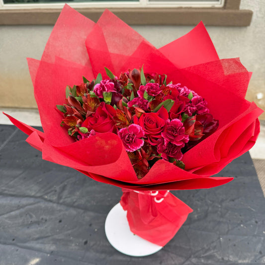 Deep red January Garnet bouquet featuring roses, carnations, and seasonal blooms wrapped in vibrant red paper, inspired by the garnet birthstone.