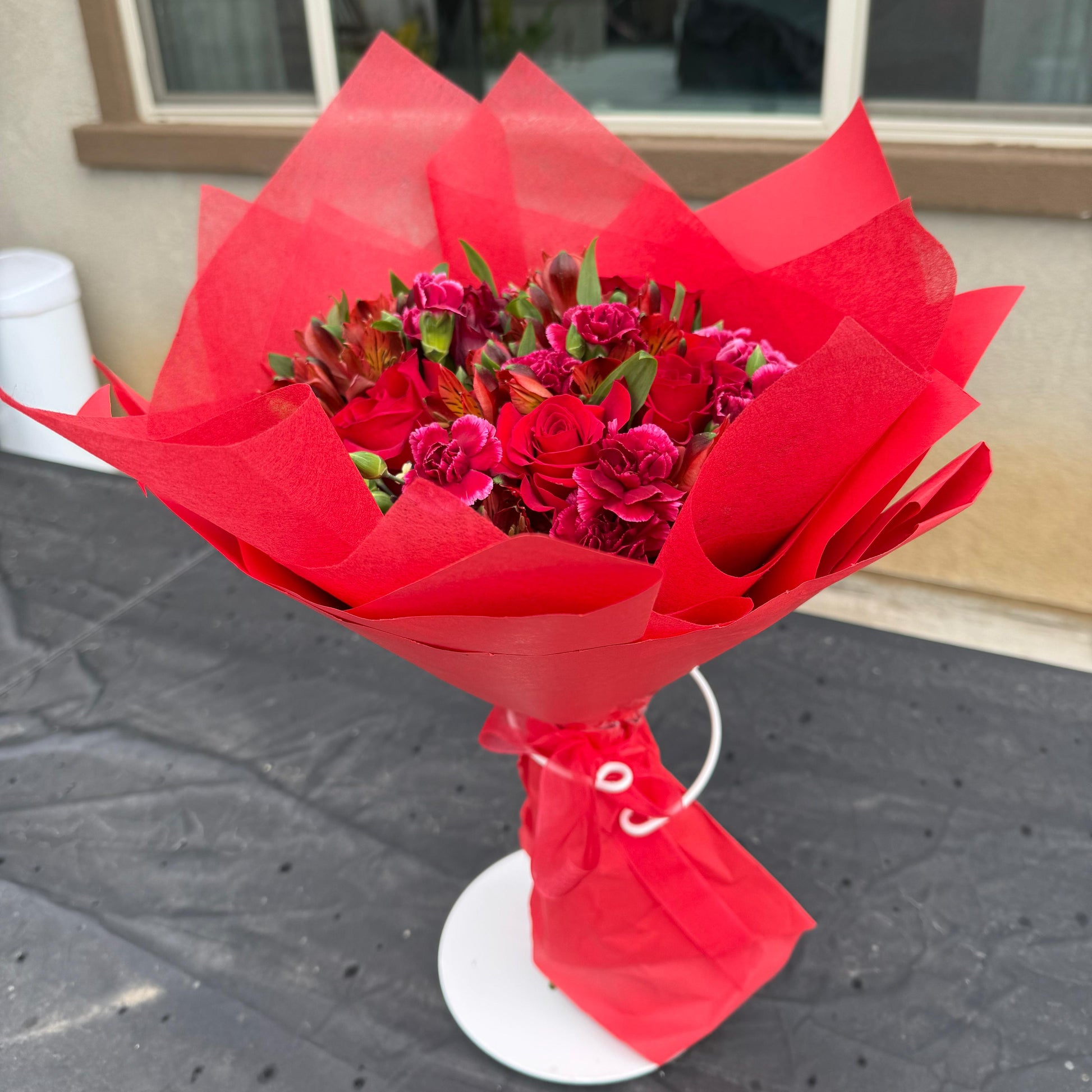 Deep red January Garnet bouquet featuring roses, carnations, and seasonal blooms wrapped in vibrant red paper, inspired by the garnet birthstone.