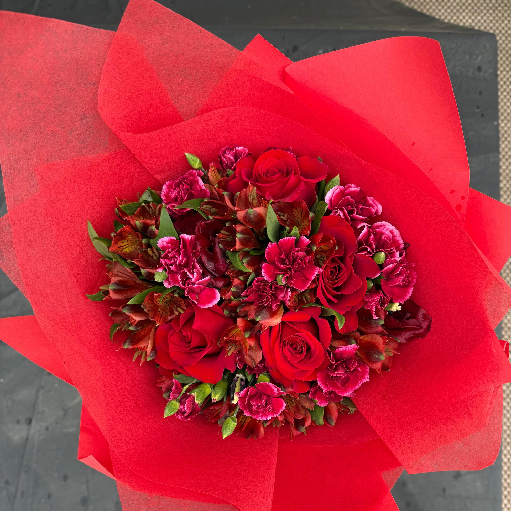 Deep red January Garnet bouquet featuring roses, carnations, and seasonal blooms wrapped in vibrant red paper, inspired by the garnet birthstone.