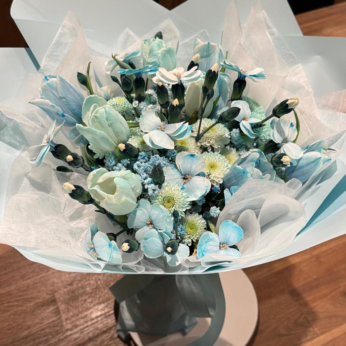 Aquamarine-inspired bouquet wrapped in soft ivory tissue and blue paper with satin ribbon.