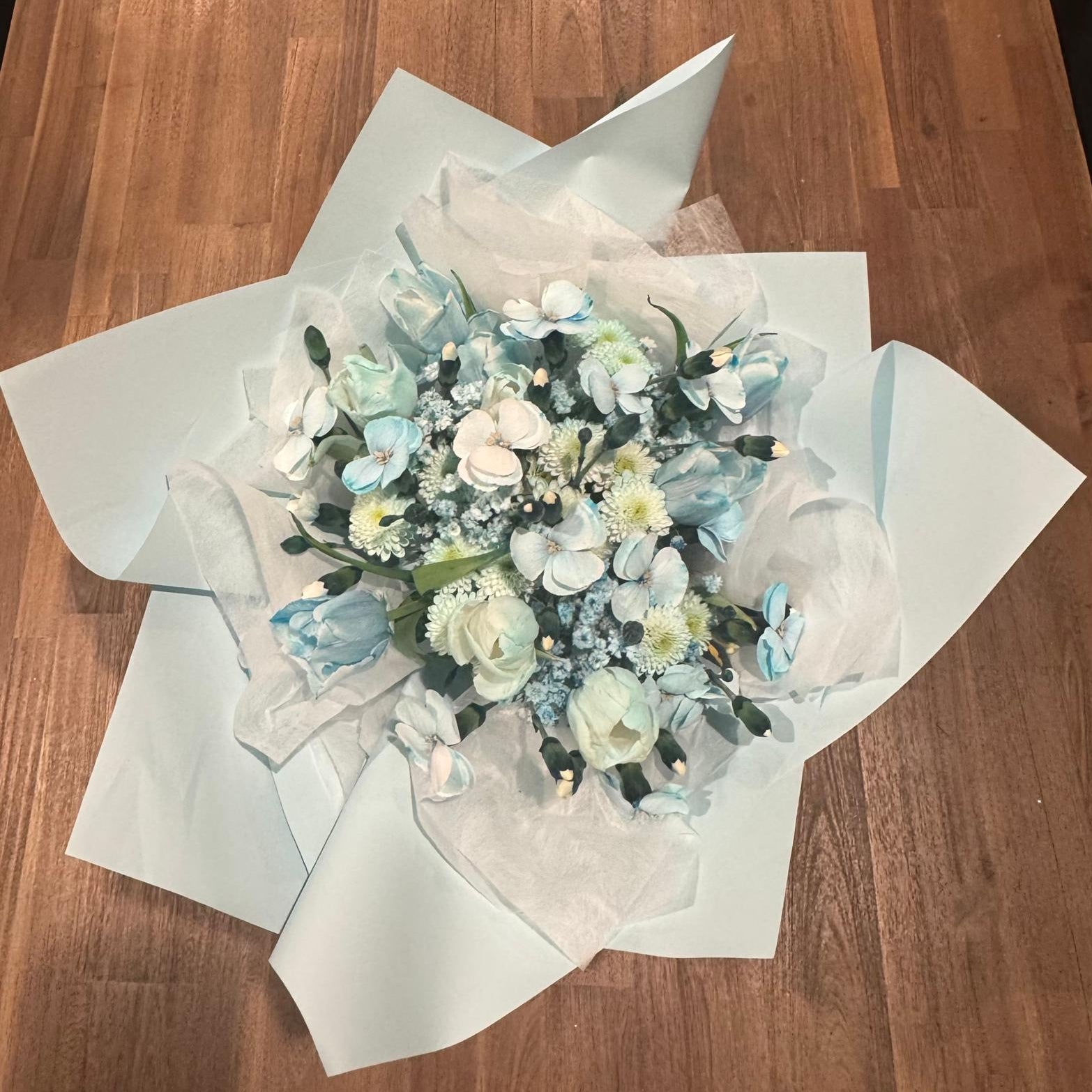 Aquamarine-inspired bouquet wrapped in soft ivory tissue and blue paper with satin ribbon.