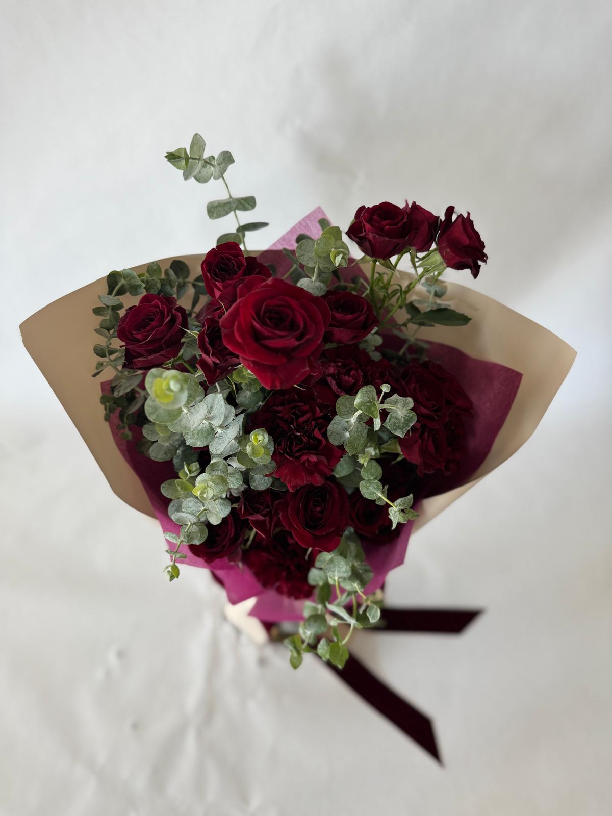 Burgundy bouquet with deep red roses and carnations, accented by eucalyptus and wrapped in plum paper with a rich, romantic look.