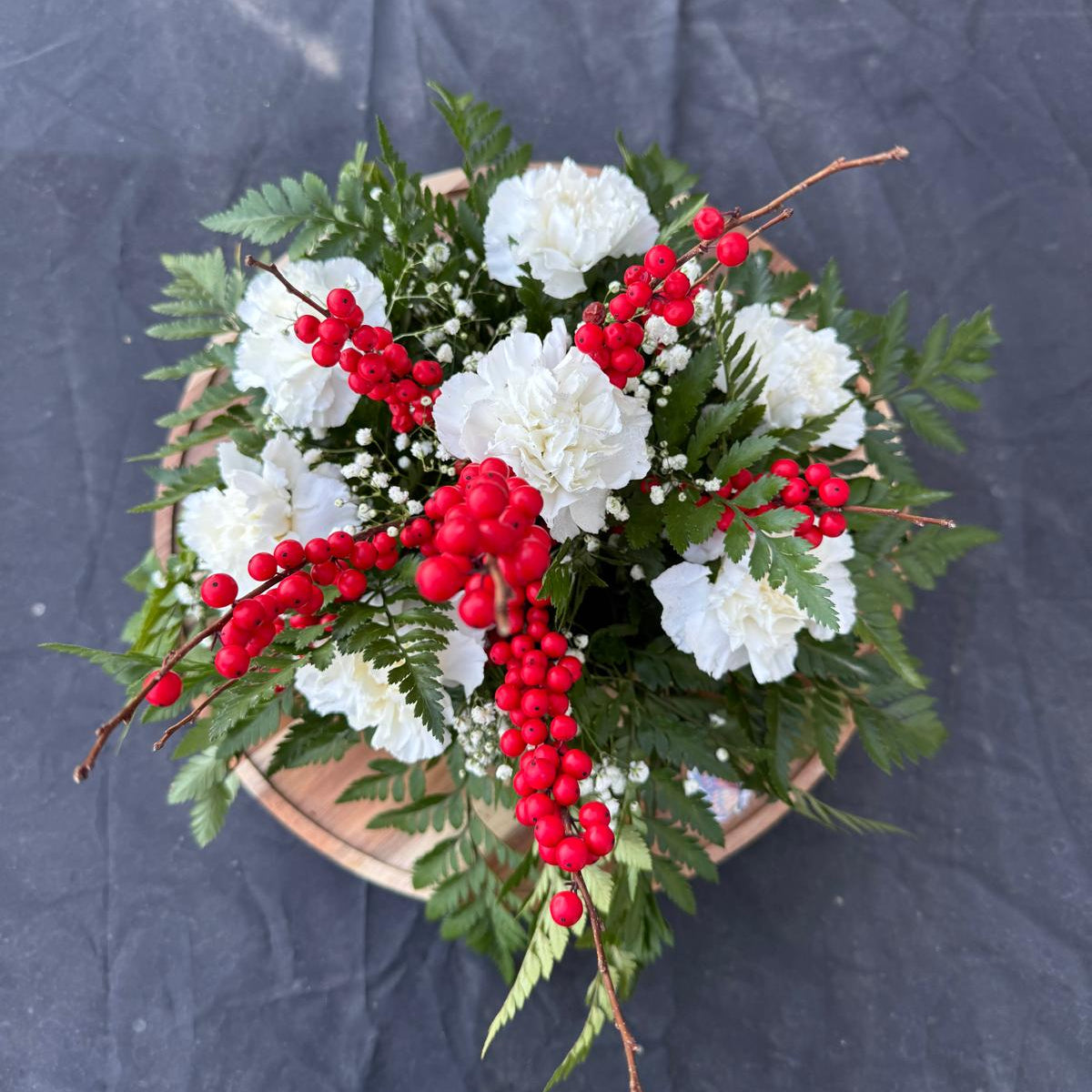 Christmas centerpiece with white flowers, red berries, baby’s breath, and greenery arranged in a low round base — Merry & Bright by Nai Pascoal Bouquets.