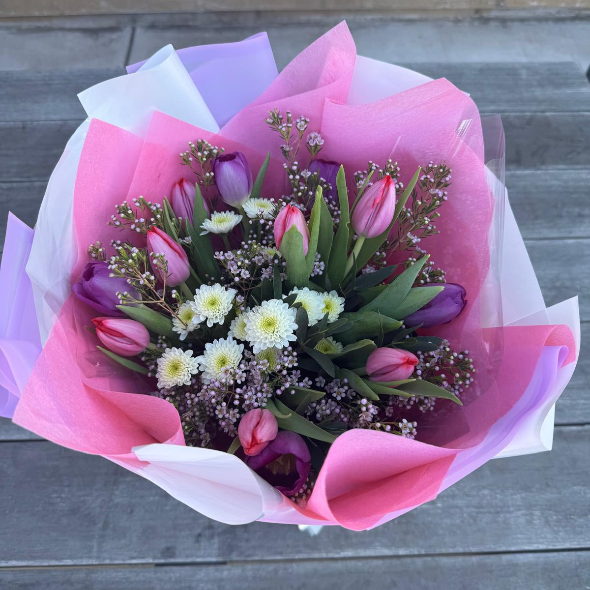 Spring bouquet with pink and lavender tulips, white chrysanthemums, and wax flower wrapped in blush and lilac pastel paper.