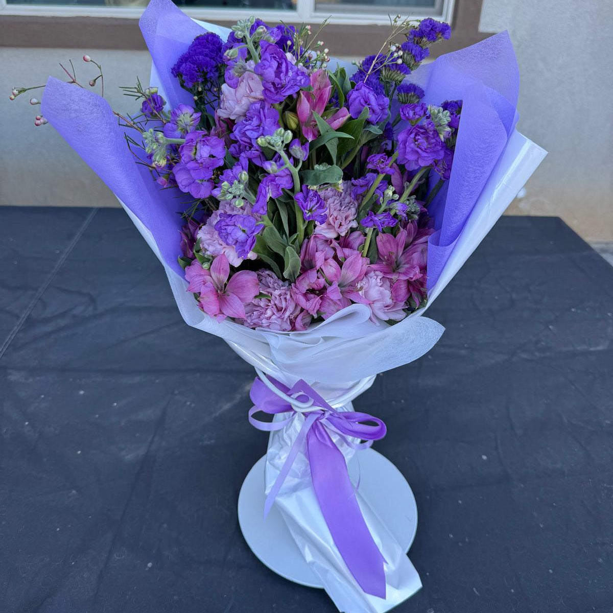 Purple and lavender February bouquet featuring stock, carnations, alstroemeria, and statice wrapped in soft lavender paper.