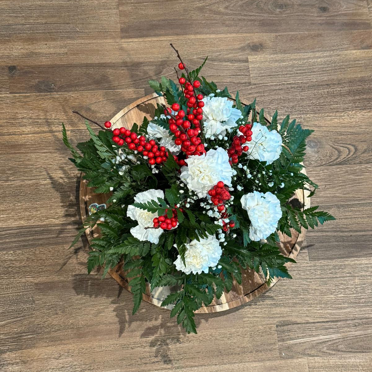 Christmas centerpiece with white flowers, red berries, baby’s breath, and greenery arranged in a low round base — Merry & Bright by Nai Pascoal Bouquets.
