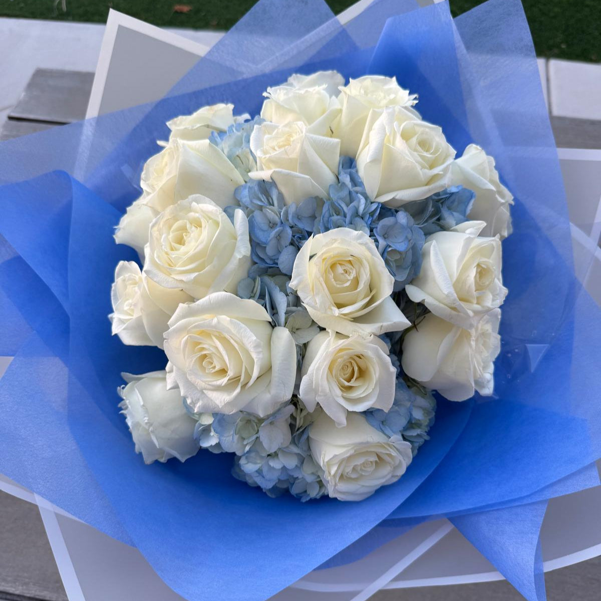 Blue and white bouquet with roses and hydrangeas, wrapped in designer paper with bold blue accents.