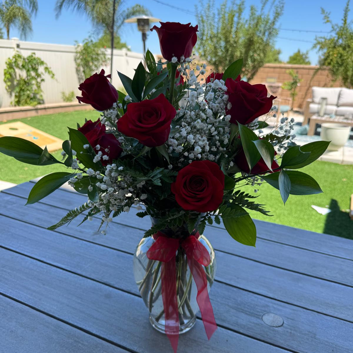Elegant vase arrangement of 12 red roses with baby’s breath and greenery, finished with a red bow.
