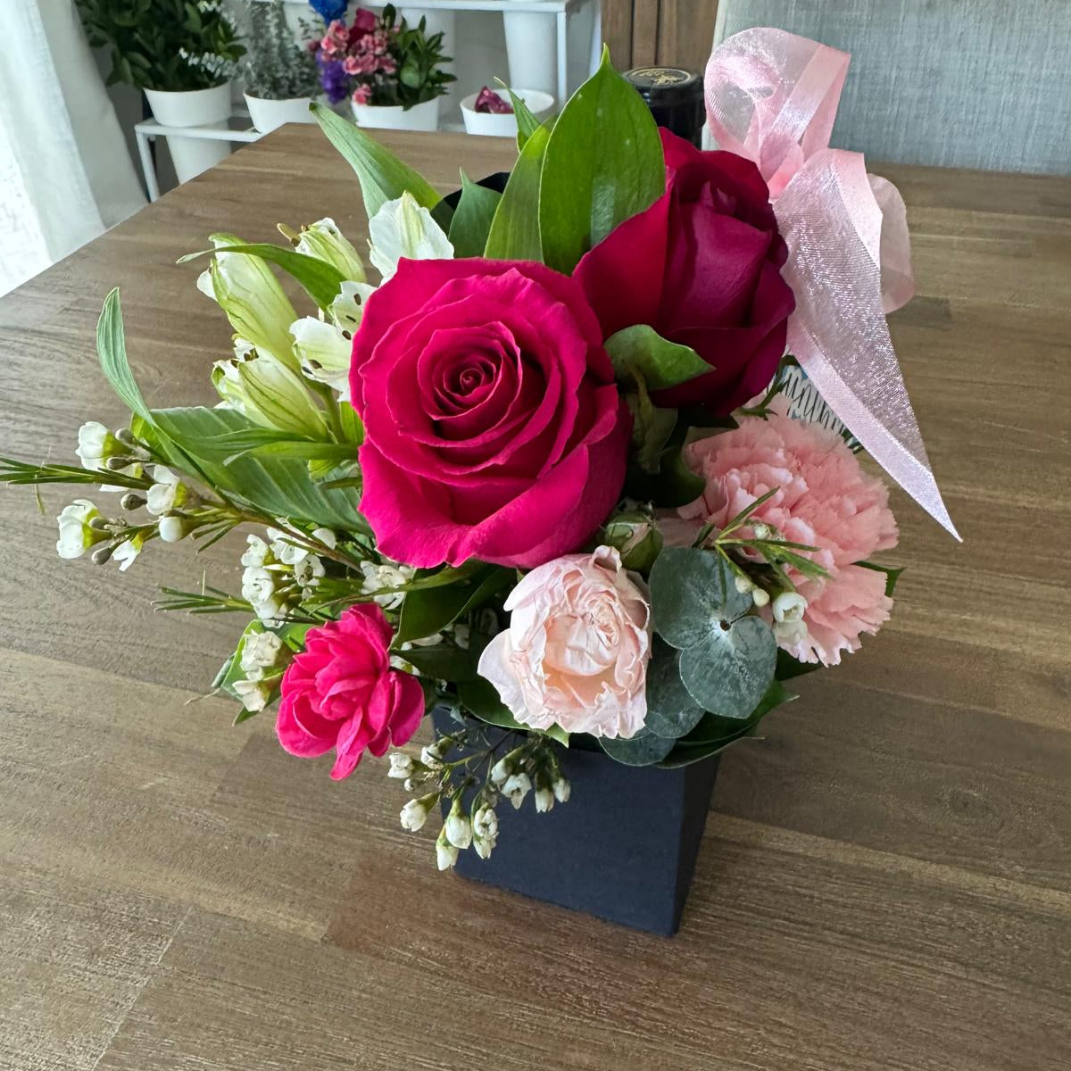 Custom floral party favor in a gift carrier with roses, carnations, and ribbon.